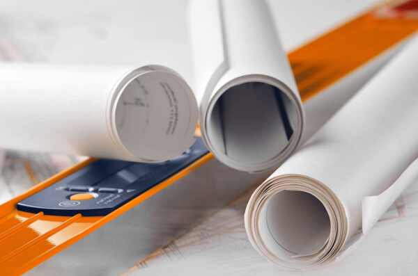 Rolled architectural blueprints on a desk with an orange ruler.