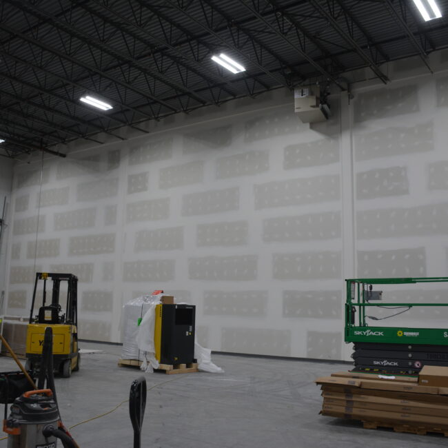 Warehouse interior with forklifts and stacked wooden pallets under industrial lighting.