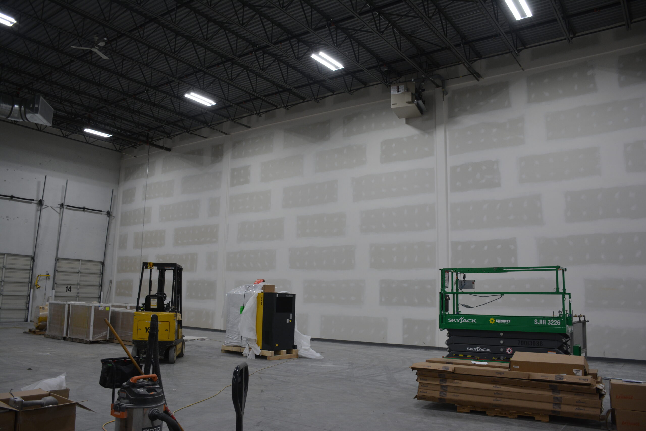 Warehouse interior with forklifts and stacked wooden pallets under industrial lighting.